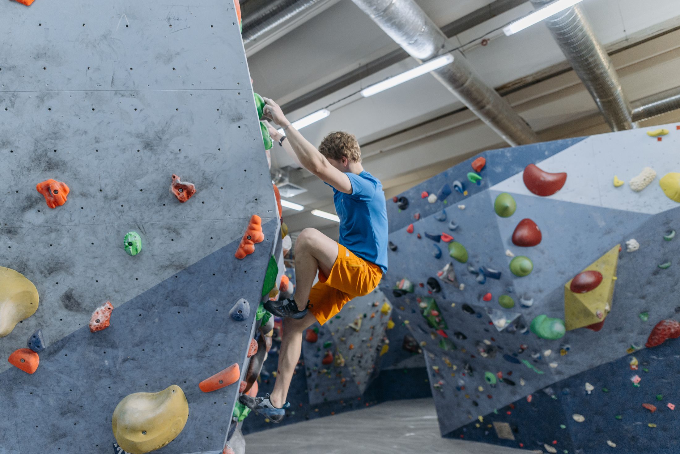 Wspinacz na szarej ścianie boulderingowej